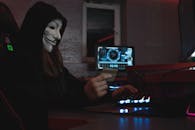 蒙面黑客在电脑前使用信用卡，象征着网络犯罪和匿名