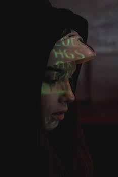A woman in a dark hoodie with digital code projected on her face symbolizes cyber security themes.