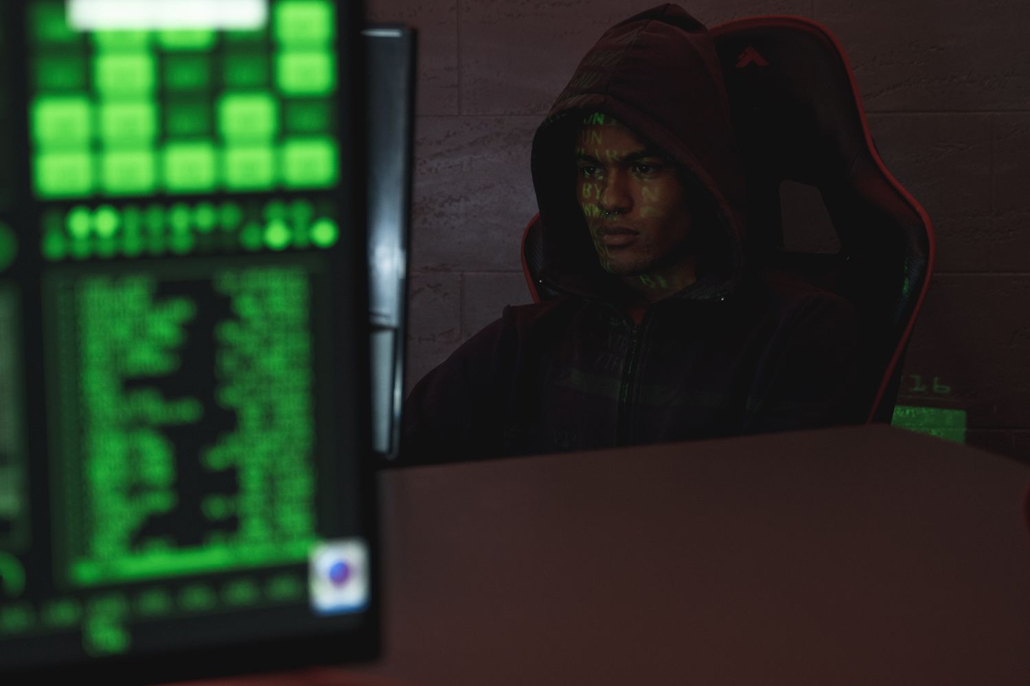 Ein Hacker in schwarzem Hoodie arbeitet an einem Computer in einem dunklen Raum, symbolisiert Cybersecurity und IT-Sicherheit.