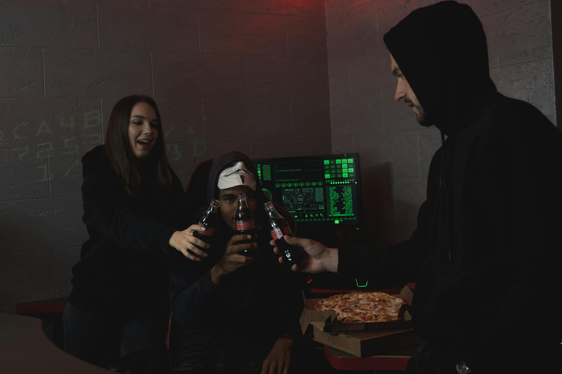 Group of hackers celebrating a successful hack with pizza and soda indoors.