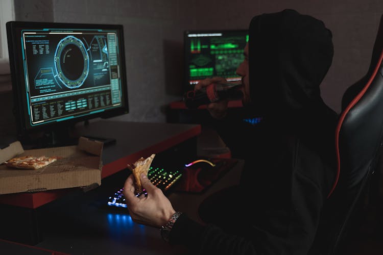 Man In Black Hoodie Eating His Snack In Front Of The Computer