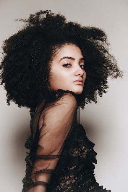 Stunning portrait of a woman with afro hair posing in a sheer black dress during a studio photoshoot.