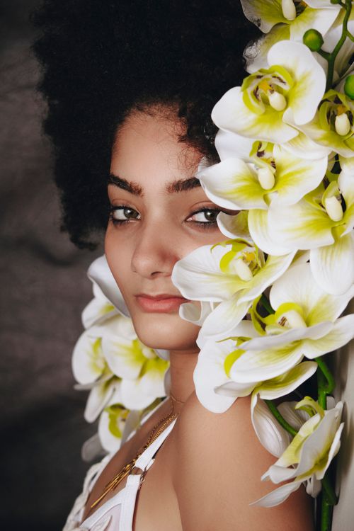 Free A serene portrait of a young woman with vibrant white and green orchids, accentuating elegance. Stock Photo