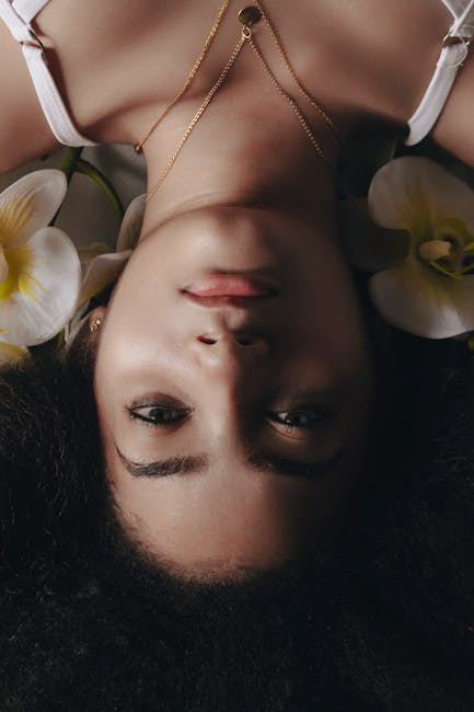 Graceful upside down portrait of a woman with gold necklace and flowers.