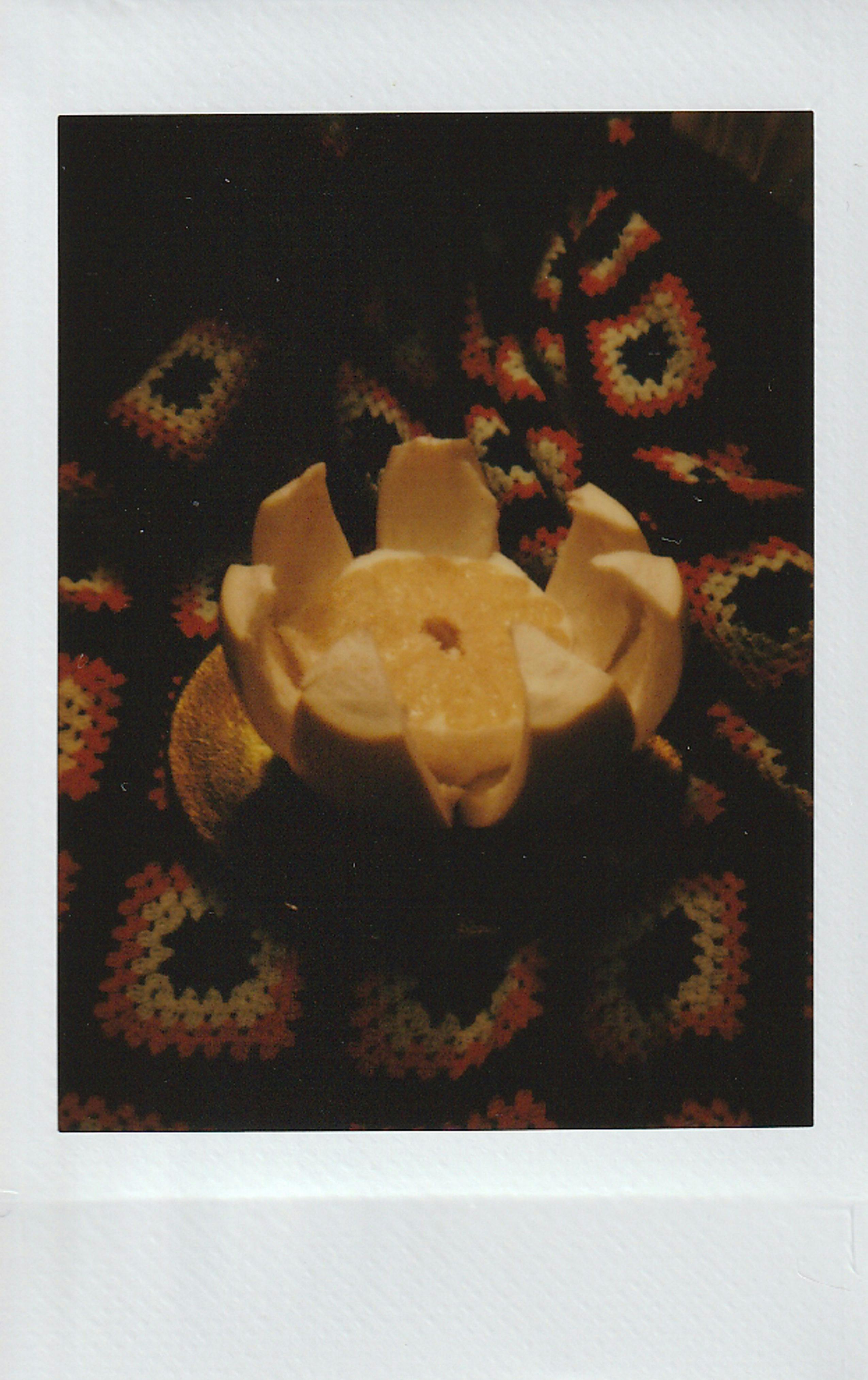 A moody, still-life Polaroid photo featuring a peeled pomelo on crochet fabric.