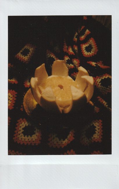 A moody, still-life Polaroid photo featuring a peeled pomelo on crochet fabric.