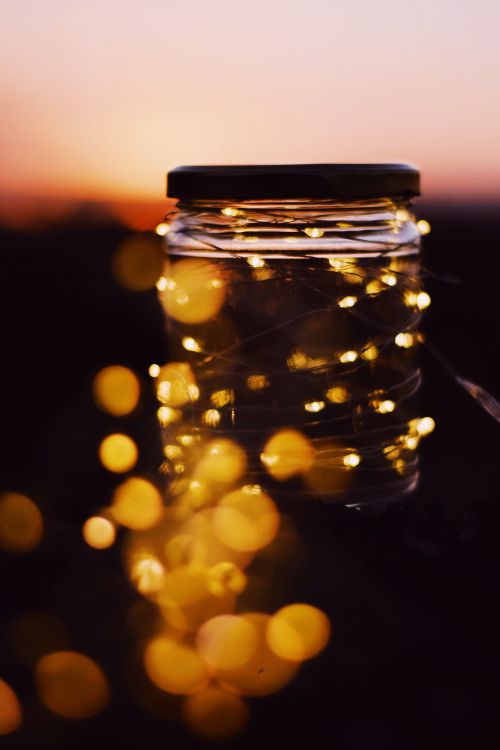 Free A serene shot of glowing string lights in a glass jar against a vibrant sunset backdrop, creating a magical ambiance. Stock Photo