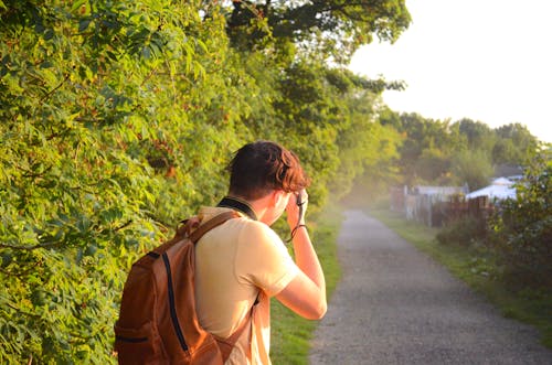 Free Back View of a Man in Brown Backpack Standing on Road Taking Pictures Stock Photo