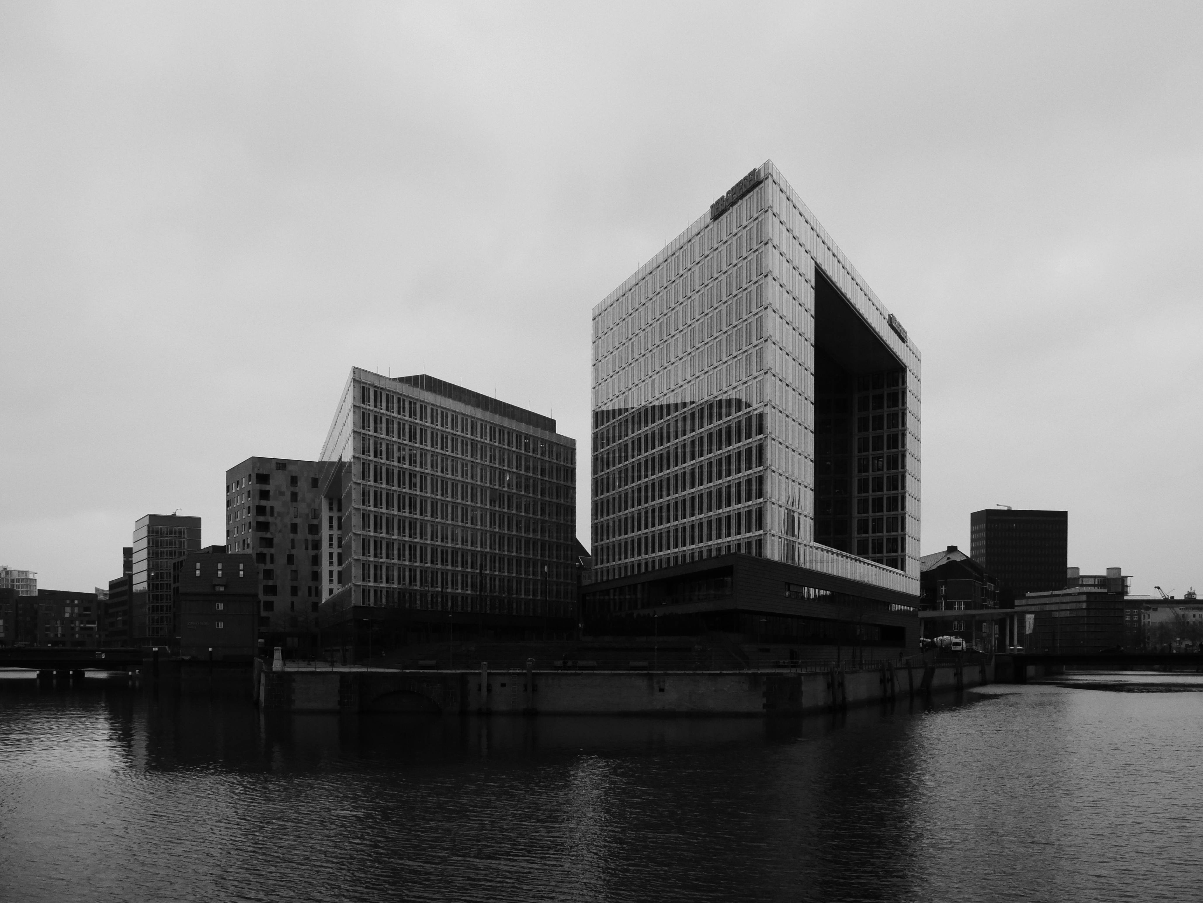 Black and white photo of modern high-rise buildings by the river in an urban cityscape.