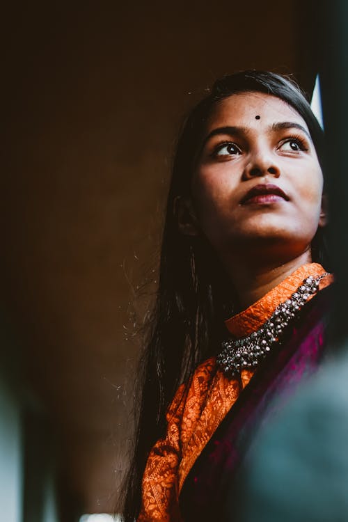 From below of young contemplative Indian lady with makeup in trendy outfit looking away