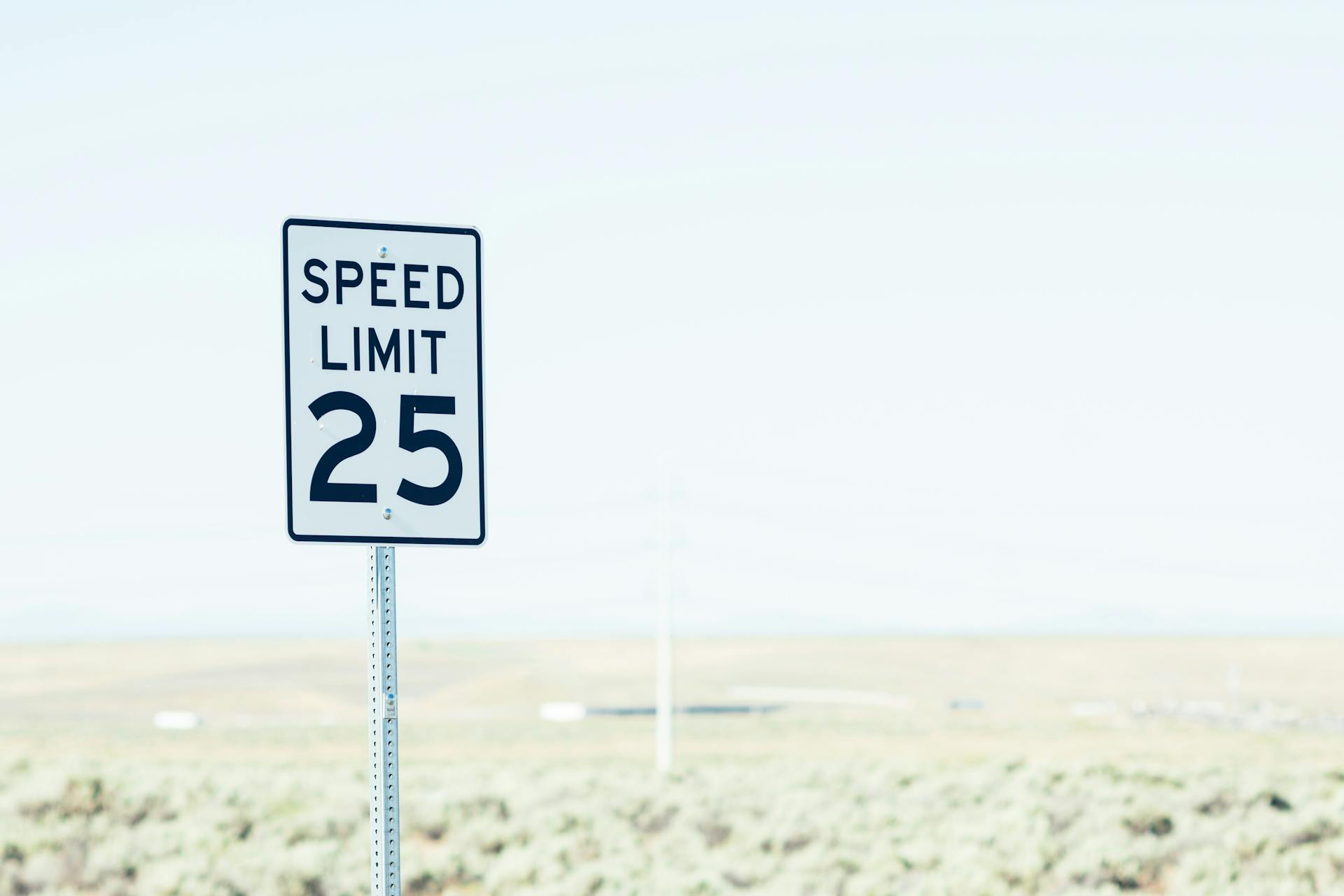 White sign on roadside with speed limit against empty green field at daytime