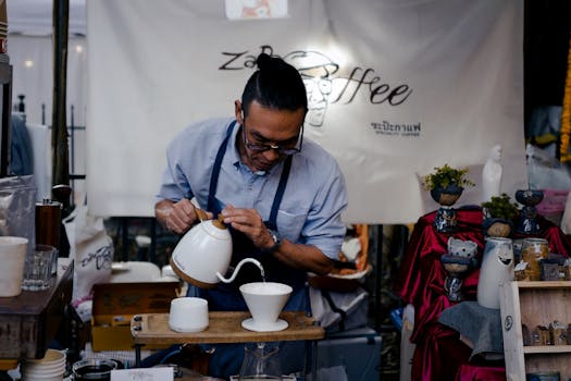 A barista skillfully pours coffee at a street market coffee stall, showcasing a traditional brewing method.
