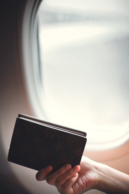 Crop faceless woman showing passport against airplane viewing window
