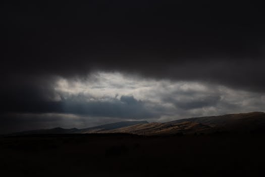 Moody clouds with sun rays over a darkened, vast rural landscape.