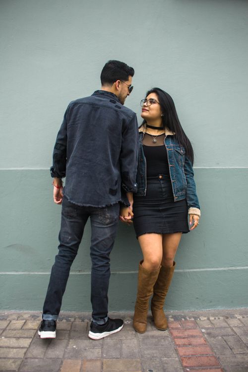 Free Trendy couple holding hands and gazing at each other against a city wall. Stock Photo