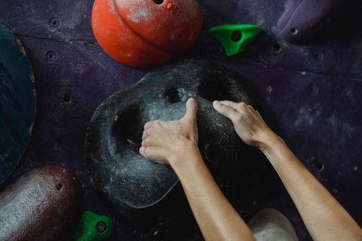 Crop anonymous female mountaineer practicing endurance and strength on climbing wall in bouldering center