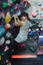 Full body back view of cheerful female alpinist climbing high on wall during active extreme training in gym