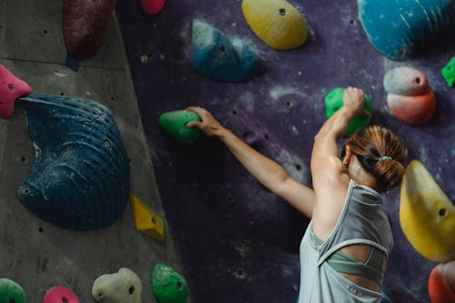 Faceless muscular sweaty female climber climbing high on wall during bouldering training in sports center