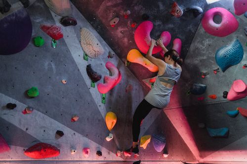 Free Back view of anonymous female athlete climbing on boulders in professional gym for mountaineering training Stock Photo