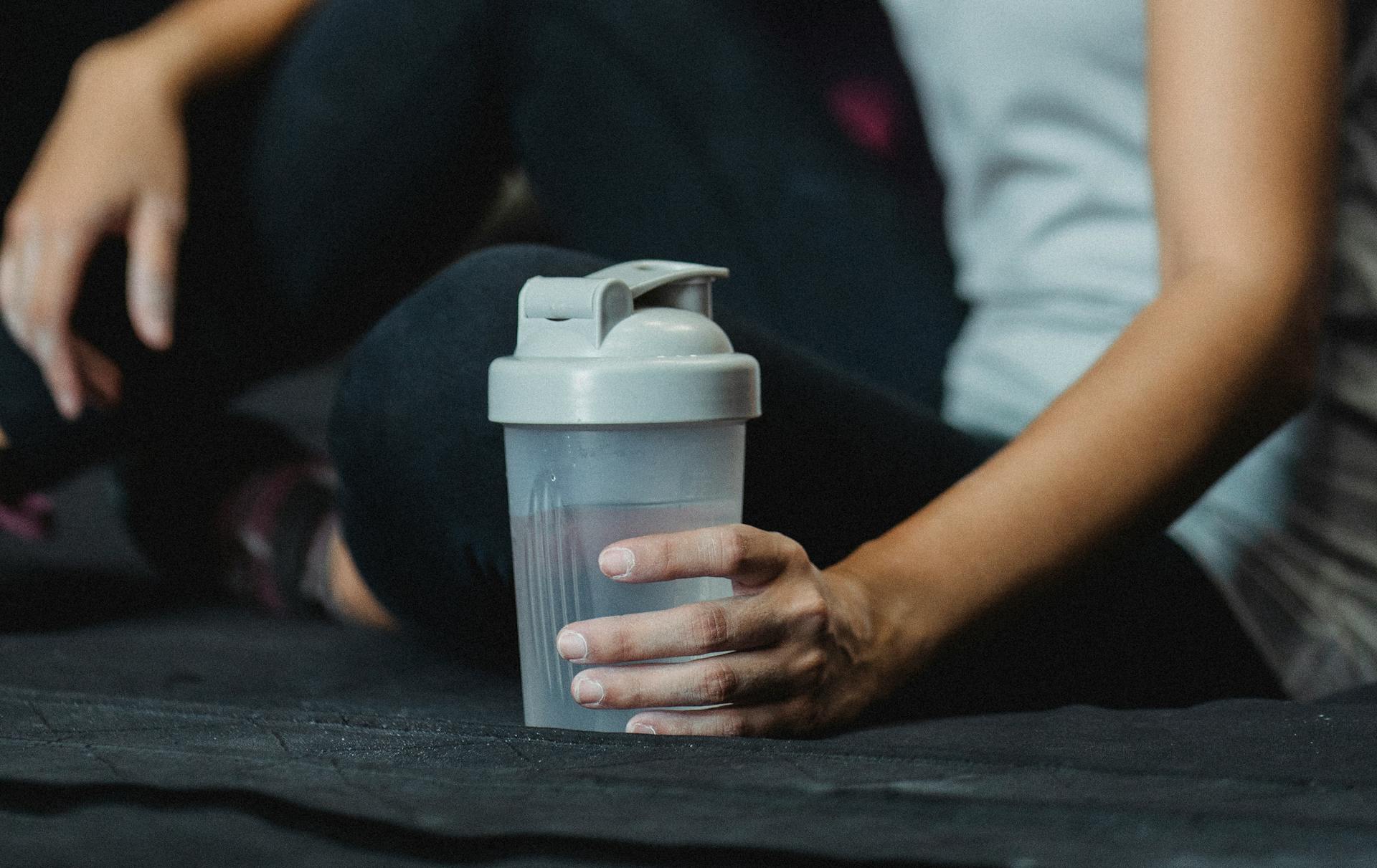 Side view crop sportswoman sitting on floor with water bottle and resting after intense training