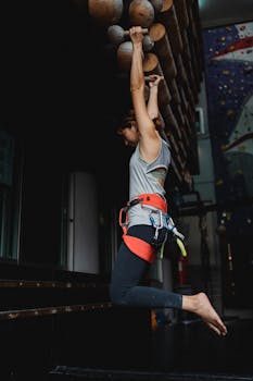 Side view full length fit sporty female in activewear and safety harness hanging on fitness bars before climbing training