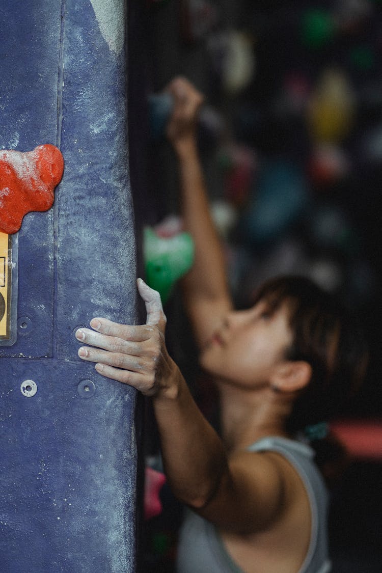 Fit Asian Woman Climbing Rock Wall In Gym