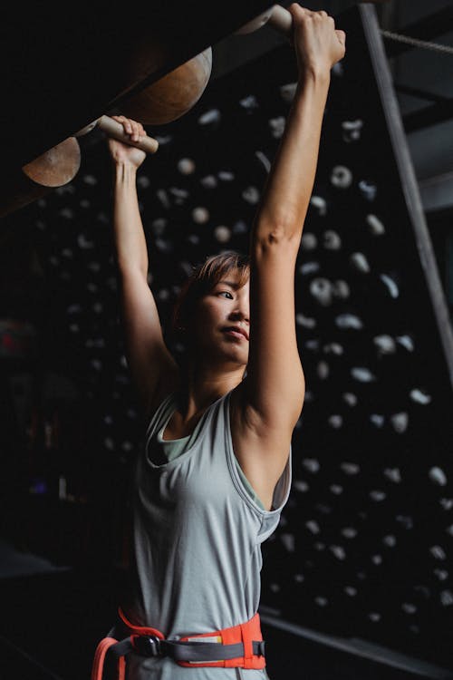 Free Positive Asian woman hanging on gymnastic equipment in climbing studio Stock Photo