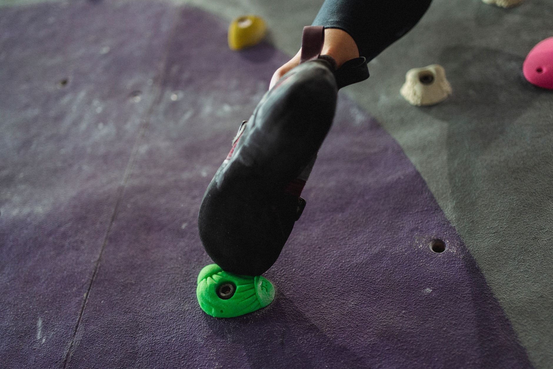 A climber's foot securely grasping a green hold on an indoor climbing wall, showcasing effort and determination.