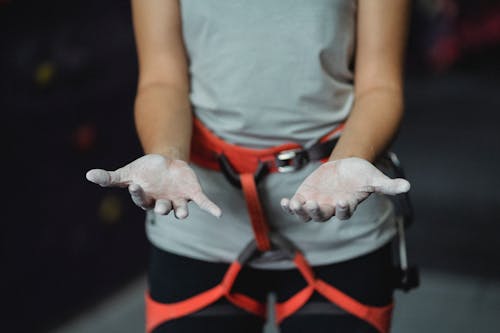 Free Crop anonymous slender female alpinist with safety harness demonstrating hands in talcum powder before practice Stock Photo