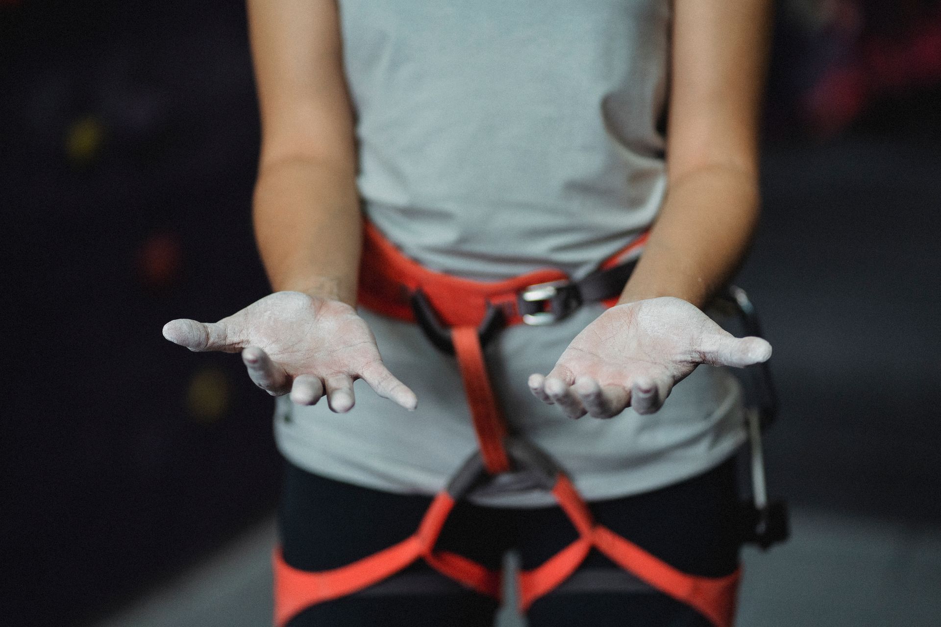 Crop anonymous slender female alpinist with safety harness demonstrating hands in talcum powder before practice