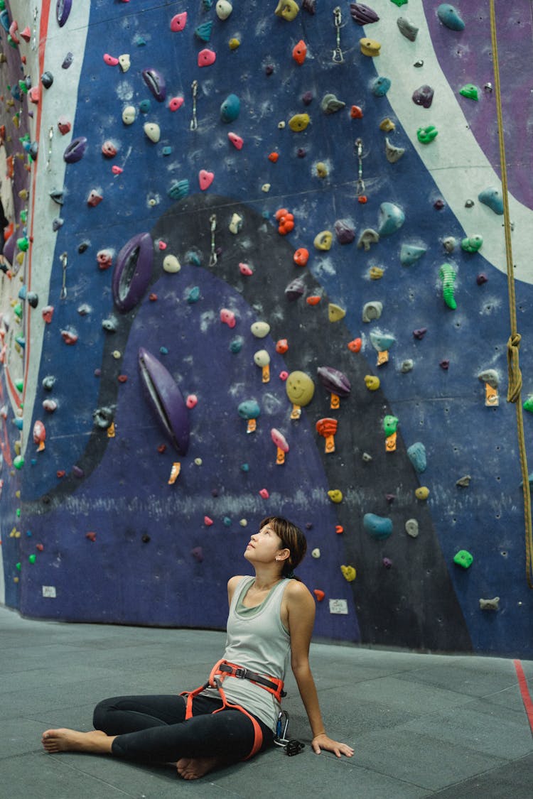 Dreamy Asian Mountaineer Resting On Floor Near Climbing Wall