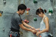 Asian trainer fastening safety harness on clothes of climber