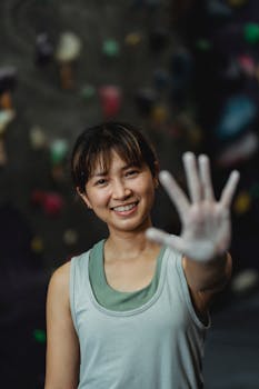 A smiling young woman climber showing her chalky hand in an indoor climbing gym.