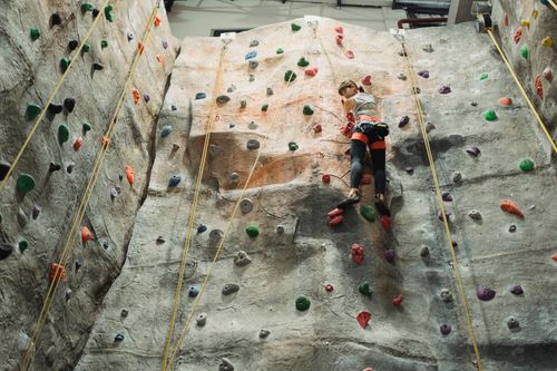 Free From below back view of young ethnic female athlete climbing artificial rock with holds while looking down Stock Photo