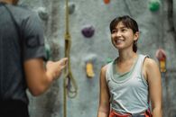Crop unrecognizable male instructor talking to cheerful fit ethnic female alpinist near climbing wall before training