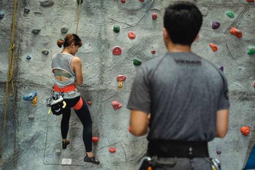 一位穿着运动服、系着安全带的匿名女性健美登山者，正在民族教练附近攀爬人造岩石的背影