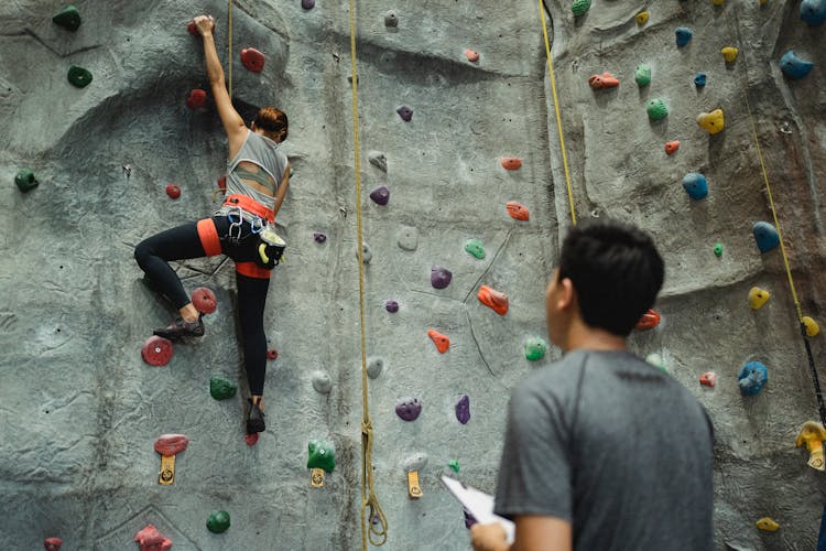 Unrecognizable Ethnic Instructor And Strong Mountaineer Climbing Rock