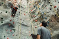 Low angle back view of unrecognizable male instructor and fit female alpinist climbing wall with holds