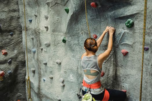 Young woman climbing on stony gray wall