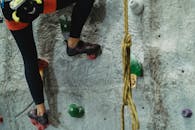 Crop anonymous risky female with belaying equipment training on stony gray climbing wall