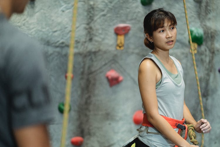 Young Asian Woman With Safety Climbing Rope Near Stony Wall