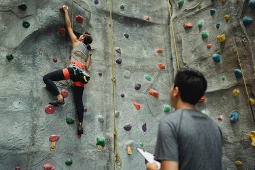 Free Back view of young female climbing wall while man writing results and watching Stock Photo
