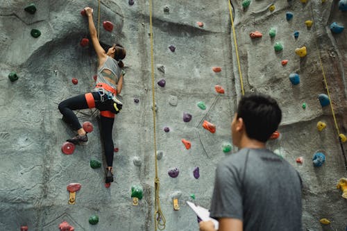 Back view of young female climbing wall while man writing results and watching