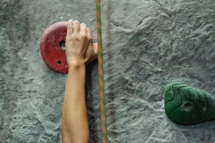 Person Touching Climbing Hold On Gray Wall