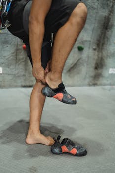 Crop anonymous male wearing special sporty climbing shoes while standing on gray surface
