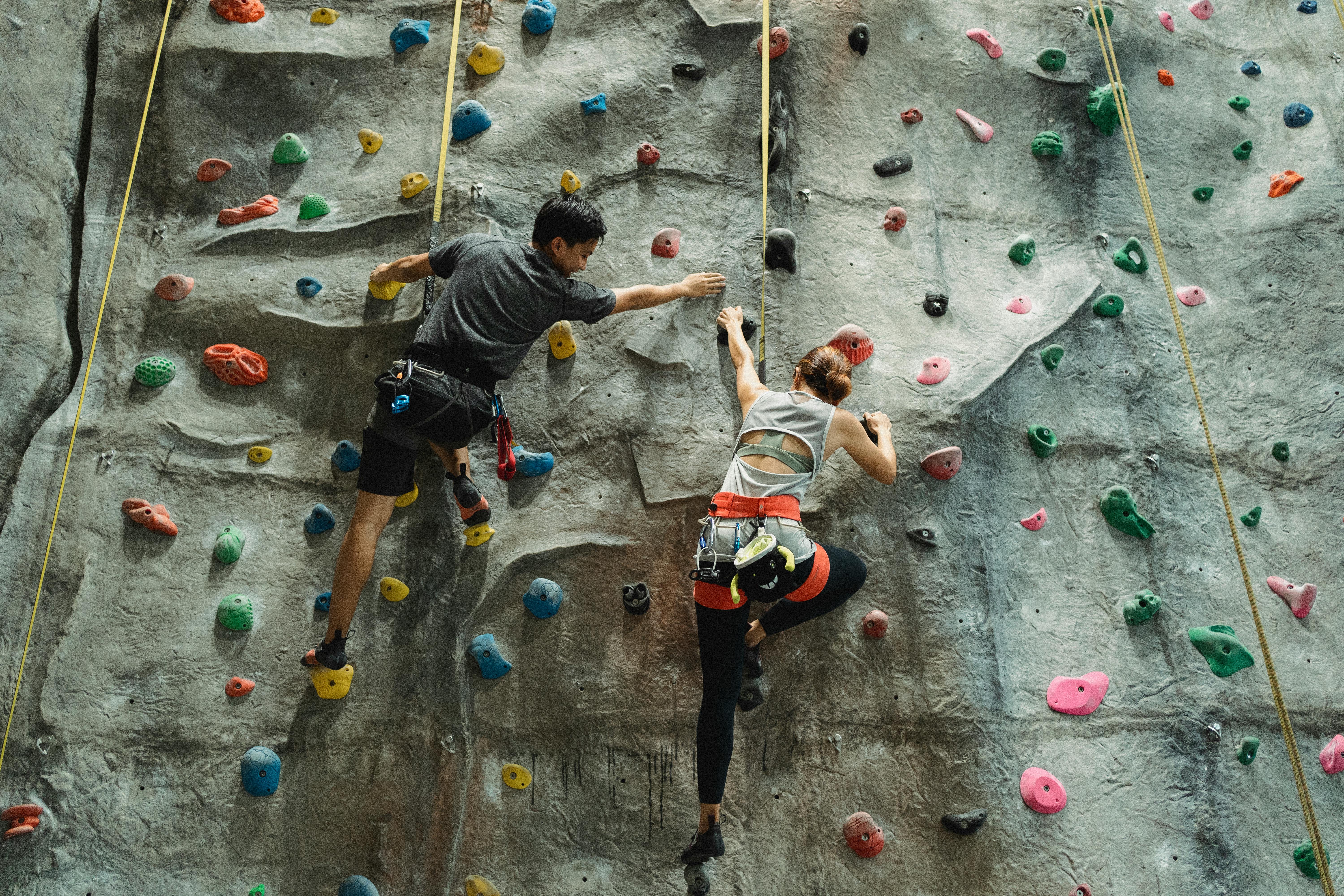 strong slim couple with safety belts climbing rocky wall