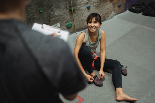 From above of cheerful ethnic female listen to coach while sitting on floor after climbing