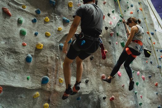 Faceless mountaineers in sportswear hanging on belays during climbing training in modern gym