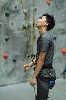 Side view of Asian male athlete holding rope while preparing for mountaineering training in climbing gym