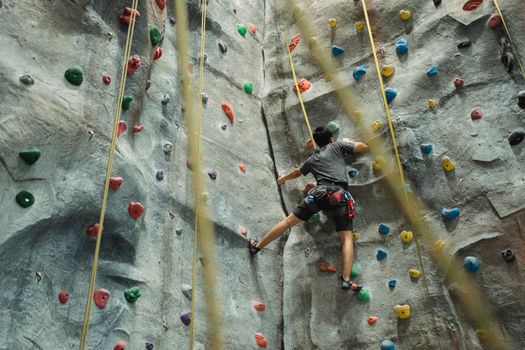 Male climber scaling an indoor rock wall with colorful holds, showcasing athleticism and focus.